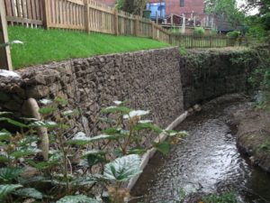 An example of a well installed gabion wall on a concrete base, alongside another gabion wall being undermined at the base and starting to fail