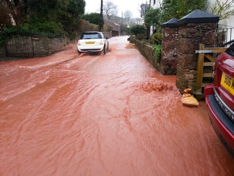A car driving through muddy flood water covering the road