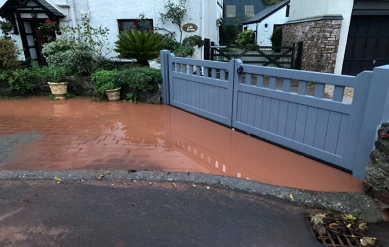 Flood gate closed across a driveway, muddy flood water has built up at the entrance but has not passed the flood gate