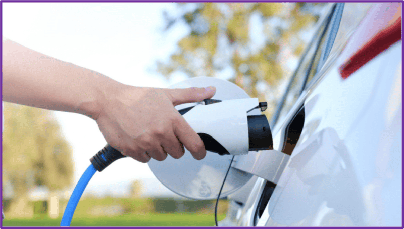 A person's hand plugging a charging cable into an electric car