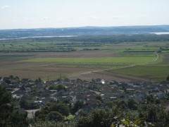A colour photograph, taken from high ground, of an open area of land in which low baulks are visible separating strips of land under differing cultivation. Some cultivation blocks are relatively large.