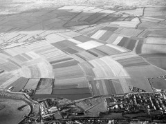 A black and white aerial photograph of an open area, covered with curving strips of different shades, indicating differing cultivation in each adjacent strip.