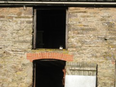 A colour photograph of a traditional farm building with a cat sitting in the hayloft opening