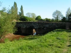 A colour photograph of a stone bridge with several arches, from the side.