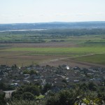 A colour photograph, taken from high ground, of an open area of land in which low baulks are visible separating strips of land under differing cultivation. Some cultivation blocks are relatively large.