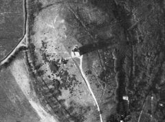 A black and white aerial photograph shows a tall, narrow building of triangular plan on a hilltop,