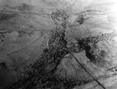 A black and white aerial photograph of a valley with sinuous earthwork ditches along the valley sides.