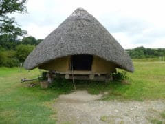 A ground photographs of a circular building with a thatched roof, raised above the ground surface by wooden posts.
