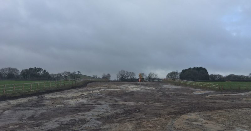 A colour ground photograph of the excavation site showing a fenced off area of land that has been stripped of topsoil.