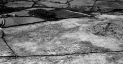 A black and white oblique aerial photograph, with rectilinear earthwork pits visible in an area of rough ground and sinuous parallel earthwork banks on the right of the frame.