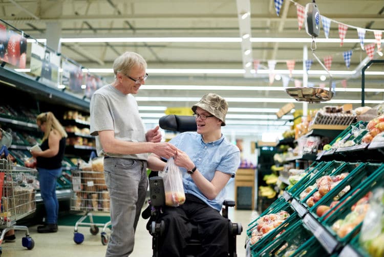 gentleman in a wheelchair being supported by his care worker while shopping in a supermarket