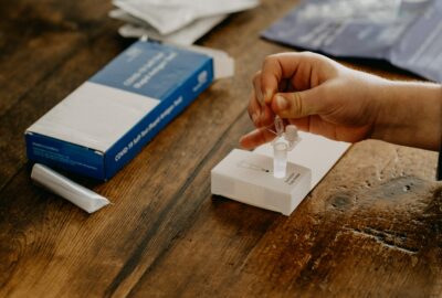 a person sat at a table taking a lateral flow test, squeezing a liquid into a small plastic tube