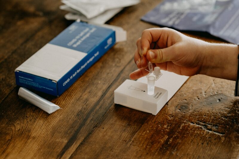 a person sat at a table taking a lateral flow test, squeezing a liquid into a small plastic tube