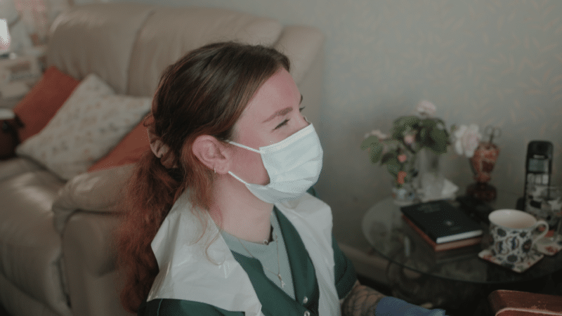 care worker, wearing a face covering, laughing with a person she cares for