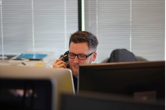 A young man working at his desk and talking on the telephone