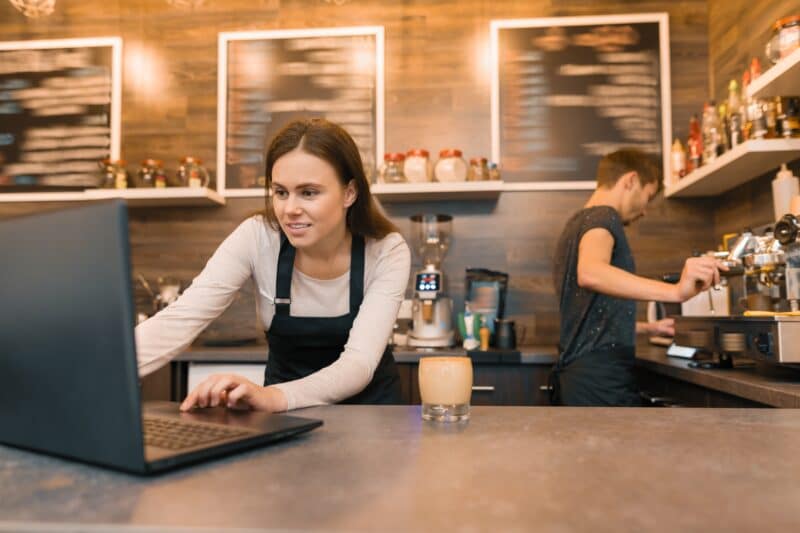 Coffee shop workers working near the counter with laptop computer and making coffee