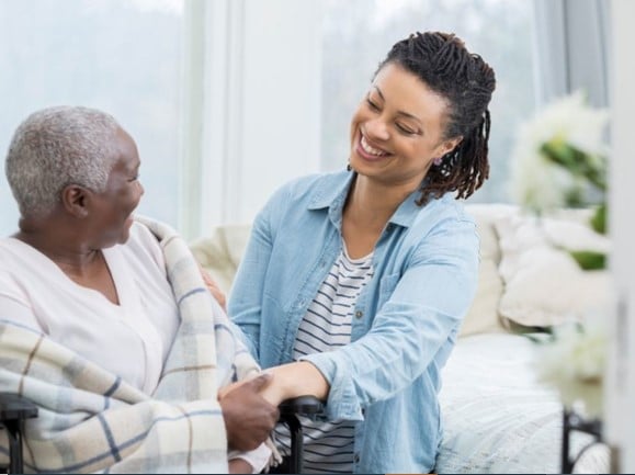 A female care worker, smiling, holding the hand of the person they are caring for.