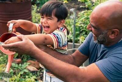 adult and child having fun watering plants in the garden
