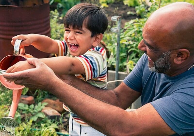 adult and child having fun watering plants in the garden