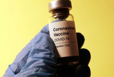 A surgical gloved hand holding a bottle of vaccine
