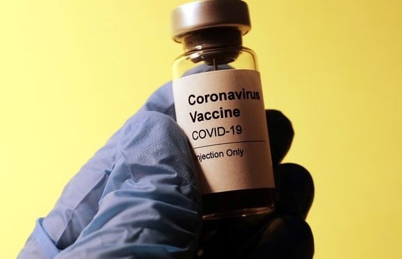 A surgical gloved hand holding a bottle of vaccine