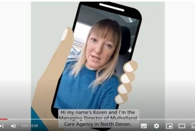 Image shows a cartoon hand holding a mobile phone. On the phone is Koren, explaining why she has had the vaccine.