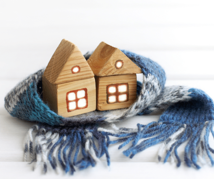 Two small model houses made of wood, huddled together with a scarf around them