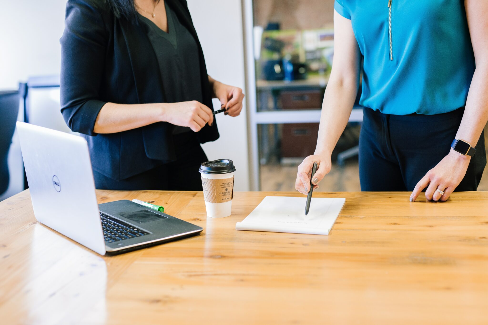 Two people stood working at a desk, with a laptop in front of them on the desk.