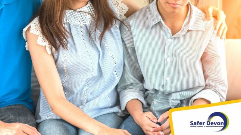 mother and son sitting by each other. Mother has arm around her son's shoulder