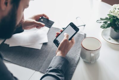 man looking at his mobile phone with his credit card in his hand