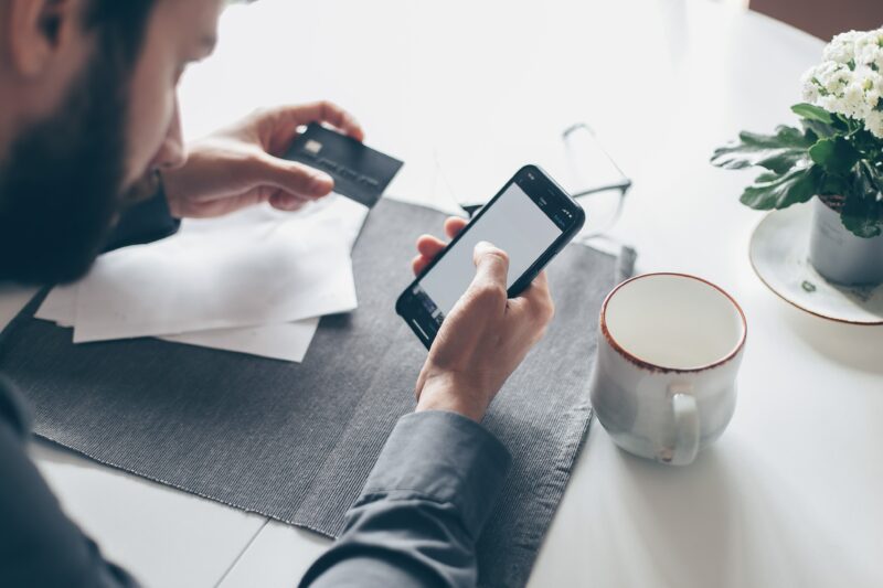 man looking at his mobile phone with his credit card in his hand