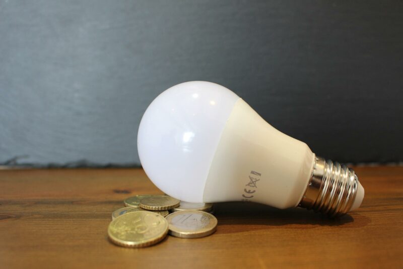 A light bulb, on a table, with some coins alongside the bulb