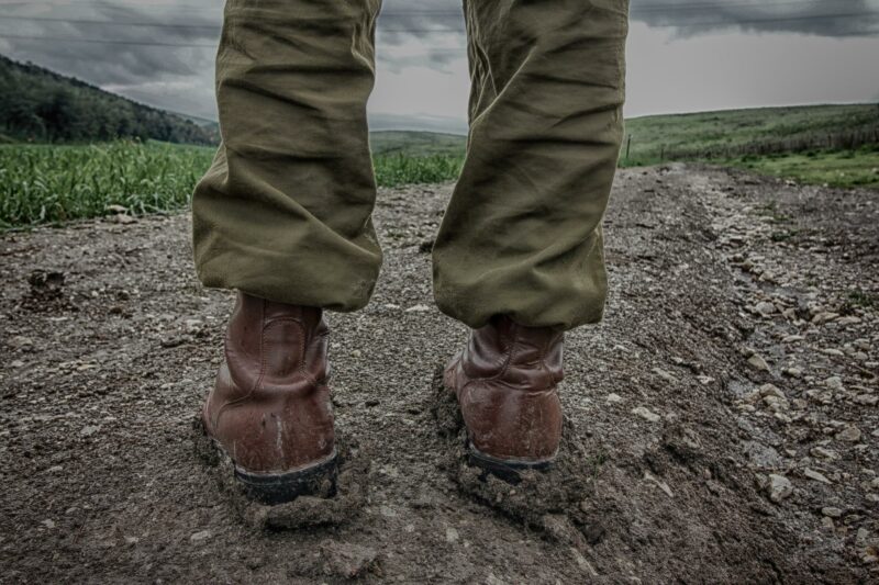 person wearing army uniform. Photo is of the knees down, with army boots visible. Person standing on a rough path.