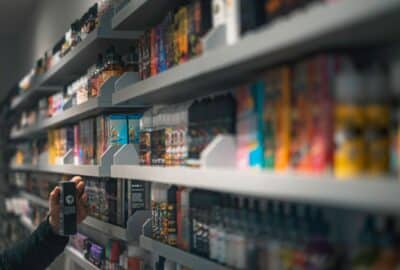 A hand reaching up to shelves containing a range of e-liquids