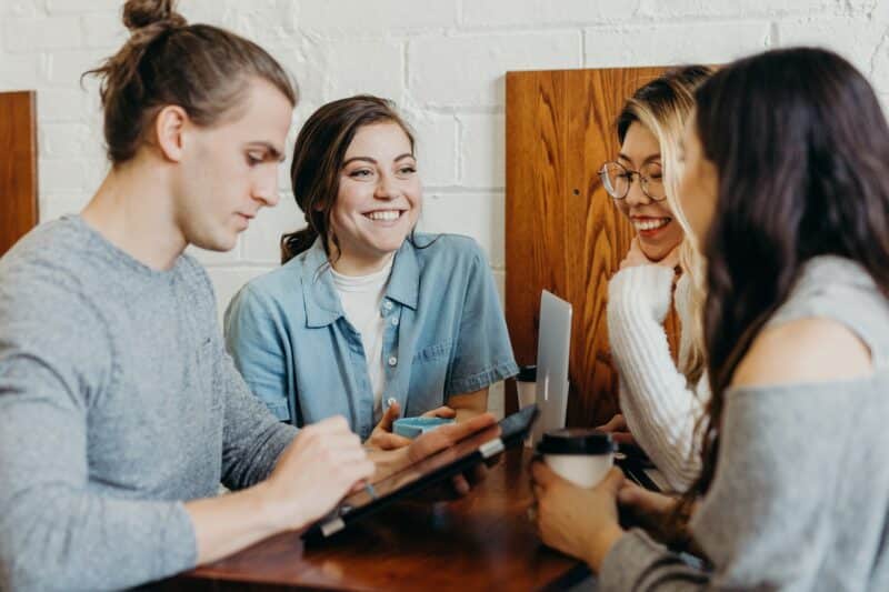 Four young people sat around a small table, with their laptops and phones, studying