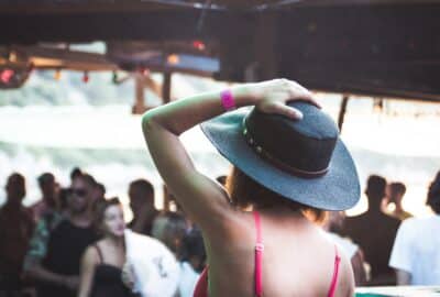 A crowd of young people at a festival, with the main person in focus wearing a large brimmed hat
