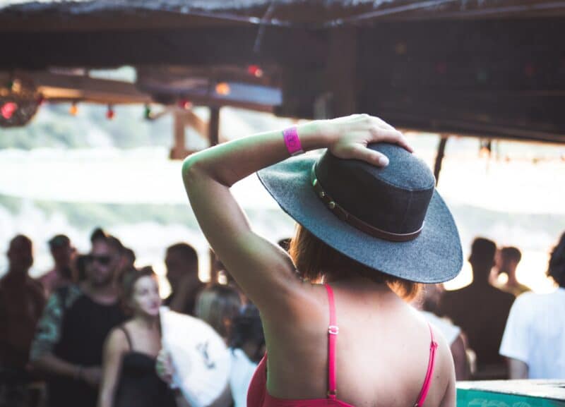 A crowd of young people at a festival, with the main person in focus wearing a large brimmed hat