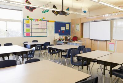 An empty school classroom, with desks and whiteboard at the front of the classroom