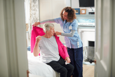 A care worker helping a lady put on her cardigan
