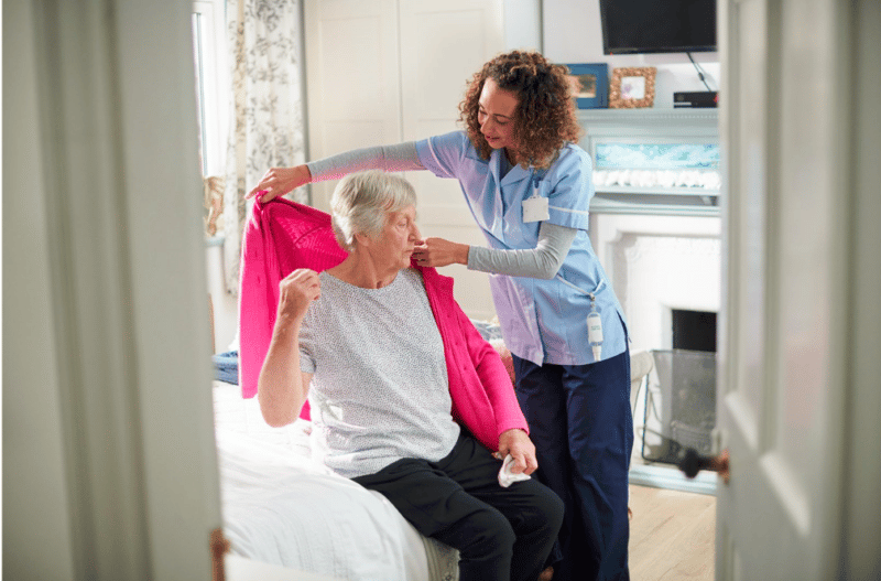 A care worker helping a lady put on her cardigan