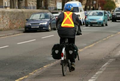Cyclist practices safety. He wears a helmet and hi-vis. He has lights on the front and back of his bike.