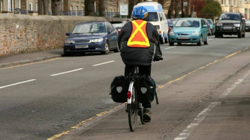 Cyclist practices safety. He wears a helmet and hi-vis. He has lights on the front and back of his bike.