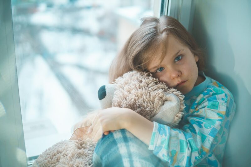 Young child sat holding her soft toy, not feeling well