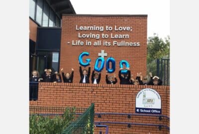 Children at Ashleigh C of E Primary School celebrating, holding up balloons that spell the word 'Good'