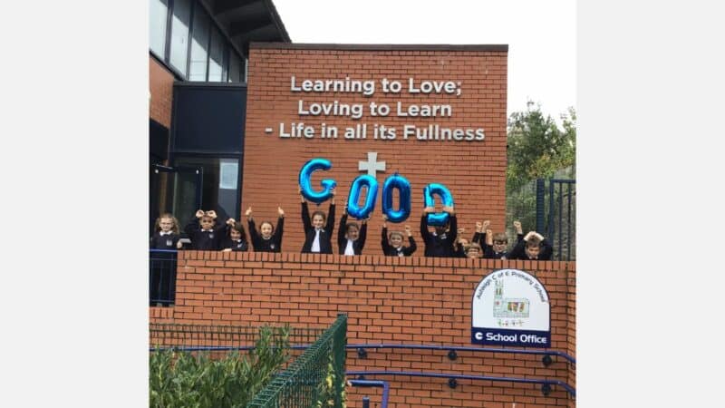 Children at Ashleigh C of E Primary School celebrating, holding up balloons that spell the word 'Good'