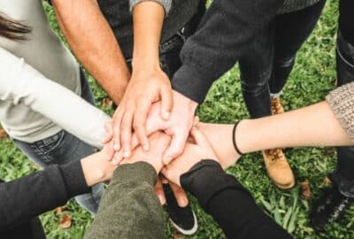 A circle of teenagers hold their hands out, with their hands together on top of each other