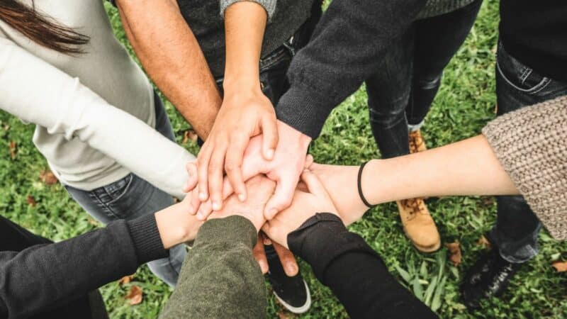 A circle of teenagers hold their hands out, with their hands together on top of each other