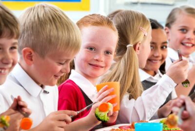 Primary school age children at school having their lunch smiling and chatting