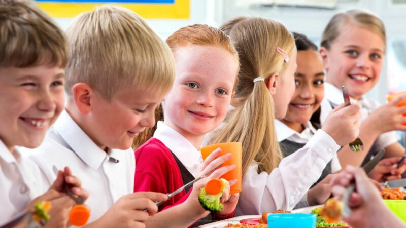 Primary school age children at school having their lunch smiling and chatting