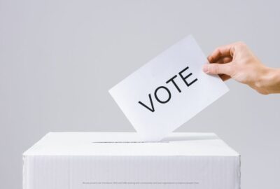 A hand placing a voting slip into a ballot box